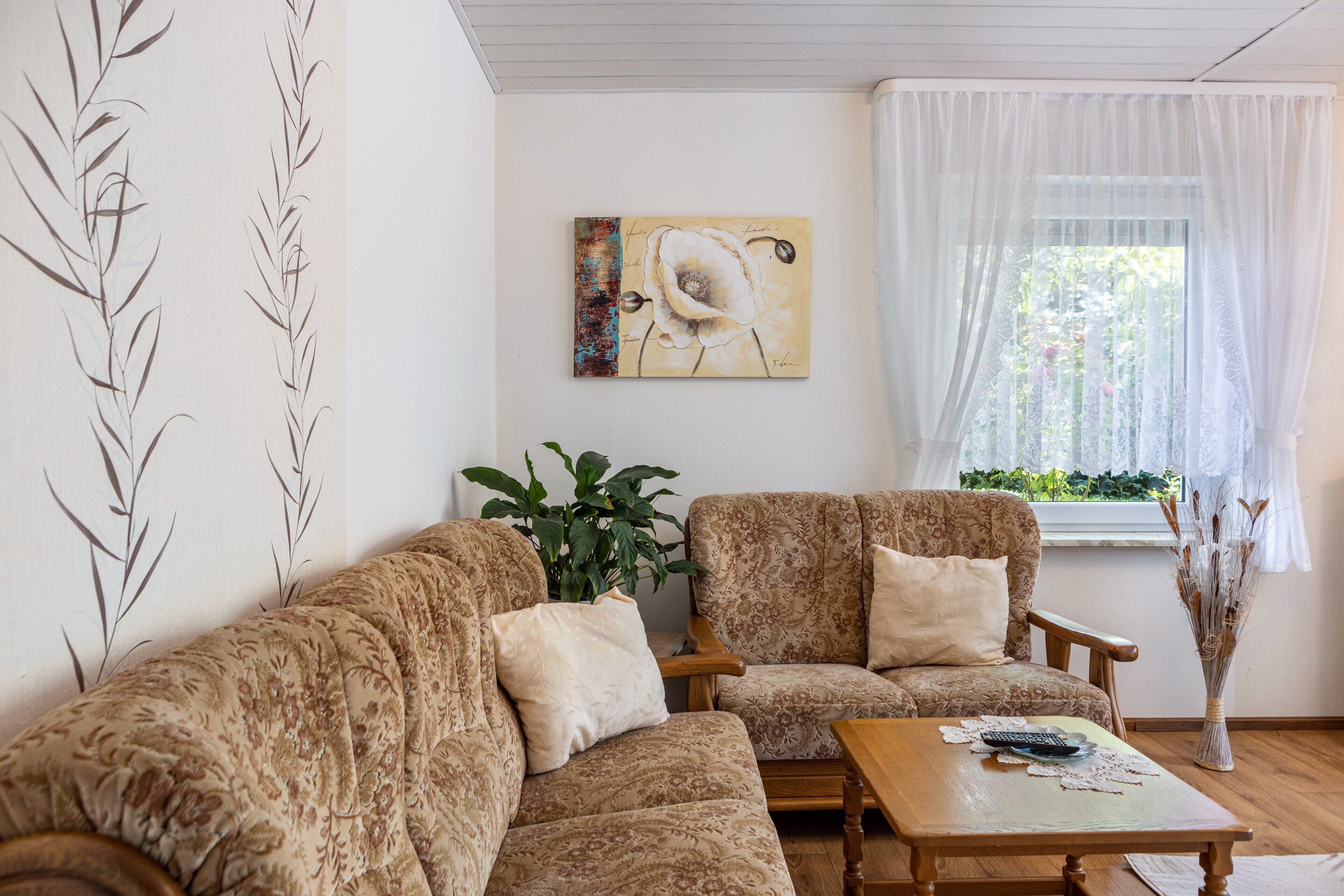 Un salon comprenant un canapé, des fauteuils, une table basse, un tableau, une plante et une fenêtre avec des rideaux.