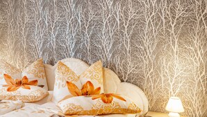 A bedroom with a patterned wallpaper, a bed with floral pillows, and a bedside lamp.