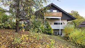 A modern two-story house with a balcony, surrounded by trees and fallen leaves.