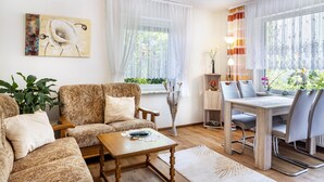 A living room with a sofa, coffee table, dining table with chairs, a lamp, and a painting on the wall.