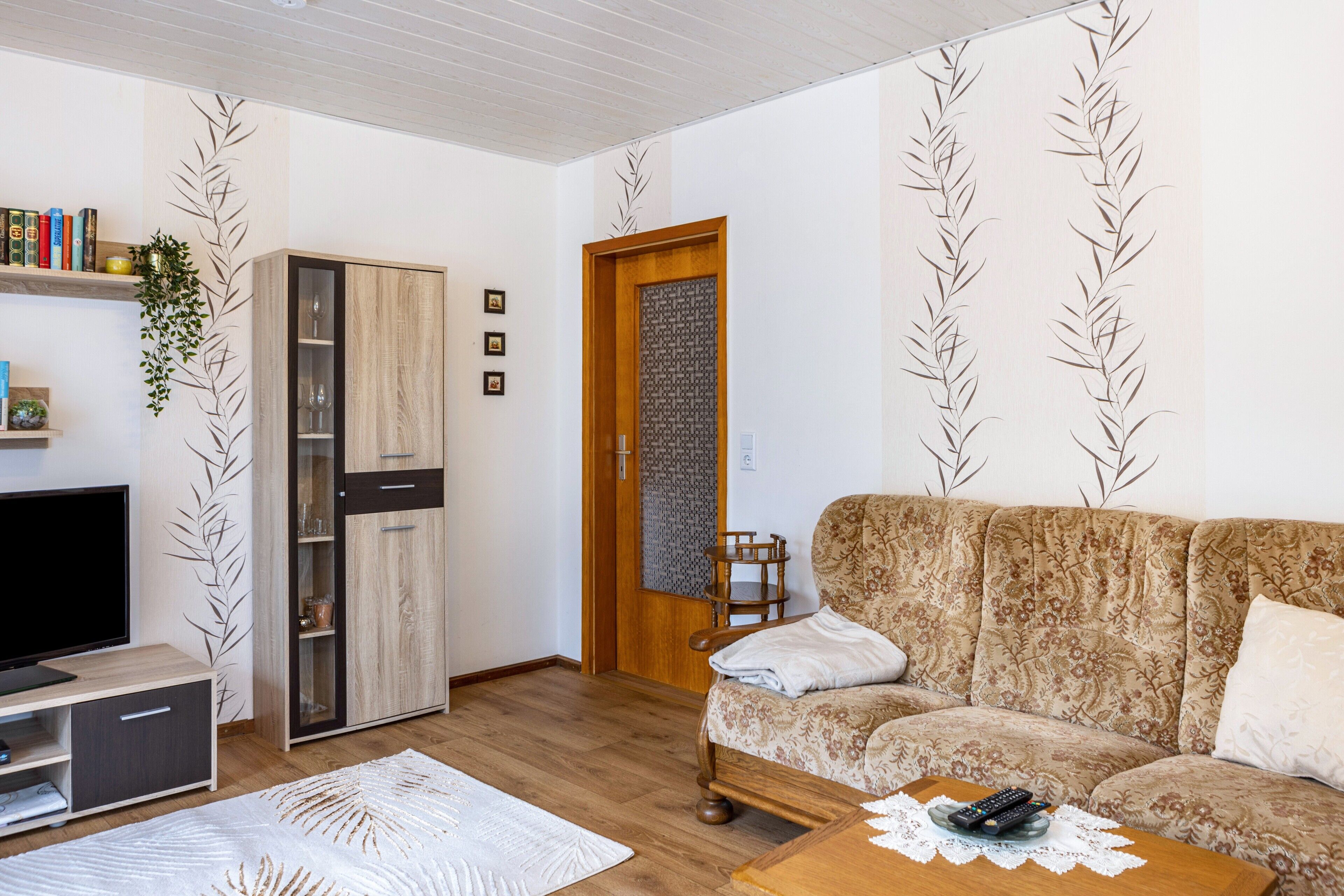 Una sala de estar con un sofá, televisor, aparador y una puerta con diseño decorativo.