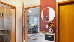 A room with a wooden door, a white cabinet with a mirror, and a dining area visible through the door.