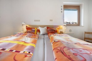 Una cama doble con ropa de cama estampada, una mesita de noche con lámpara, una ventana con vistas y una pequeña mesita de noche con un reloj.