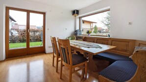 A dining area with a wooden table, chairs, and a bench. There are sliding glass doors leading to a garden. - Holiday Home 'Hilde' with Mountain View, Private Terrace and Wi-Fi (Schwangau)