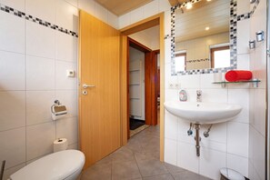 Ein Badezimmer mit Toilette, Waschbecken, Spiegel und Duschbereich.