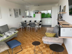 Un salon moderne comprenant un canapé, deux fauteuils, une table basse et un coin repas avec des chaises et une table.