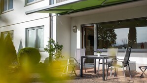 A patio with a table and chairs, a potted plant, and a building with large windows. - Apartment 'Pusteblume' with Private Terrace and Wi-Fi (Kappelrodeck)