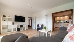A modern living room with a sofa, TV, and a small table with a vase. - Apartment 'Pusteblume' with Private Terrace and Wi-Fi (Kappelrodeck)