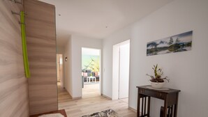 A modern interior with a wooden floor, a marble-patterned rug, a wooden bench, a dark wooden side table with a plant, and a painting on the wall. - Apartment 'Pusteblume' with Private Terrace and Wi-Fi (Kappelrodeck)