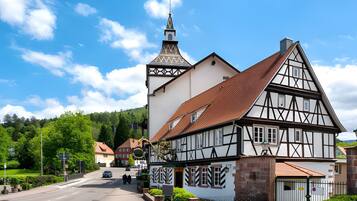 Ein traditionelles Fachwerkhäuschen mit einem markanten Turm, einem verschlossenen Eingang und einer gepflasterten Straße unter blauem Himmel.