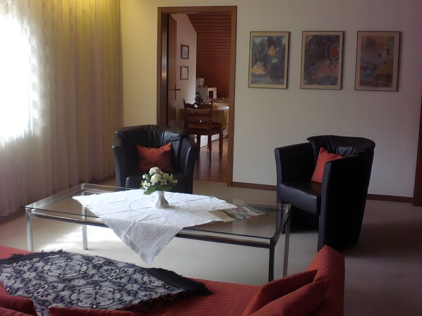 A living room with a glass coffee table, two black leather chairs, a patterned rug, and a vase with flowers.