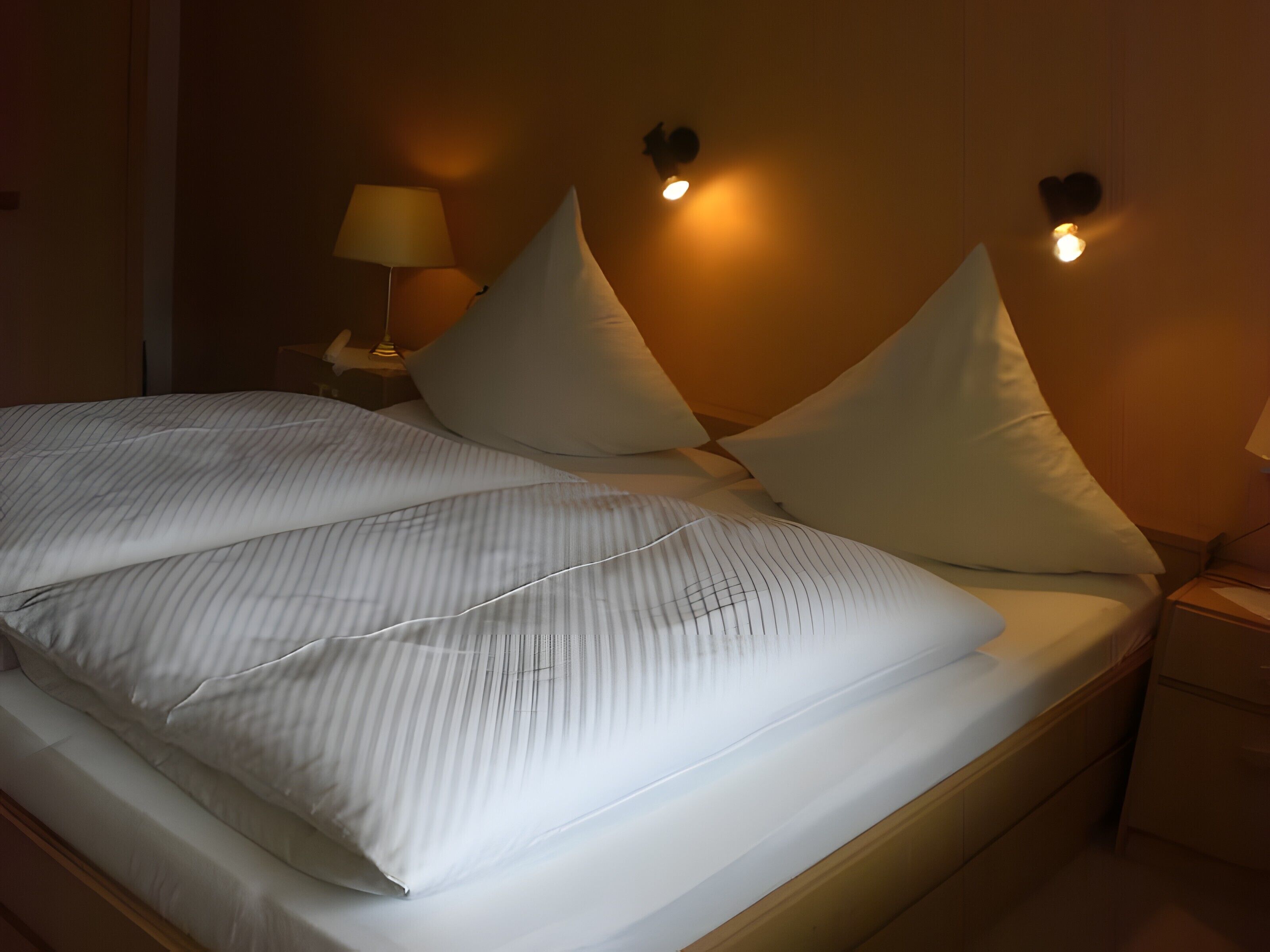 Ein ordentlich bezogenes Bett mit gestreifter Bettwäsche, zwei Nachttischlampen und einer Wandleuchte.