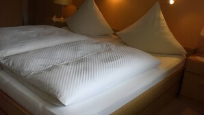 A neatly made bed with striped bedding, two bedside lamps, and a wall-mounted light fixture. - Apartment 'Nr 2, 30qm' with Private Terrace, Shared Garden and Wi-Fi (Bad Herrenalb)