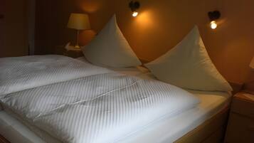 Ein ordentlich bezogenes Bett mit gestreifter Bettwäsche, zwei Nachttischlampen und einer Wandleuchte.