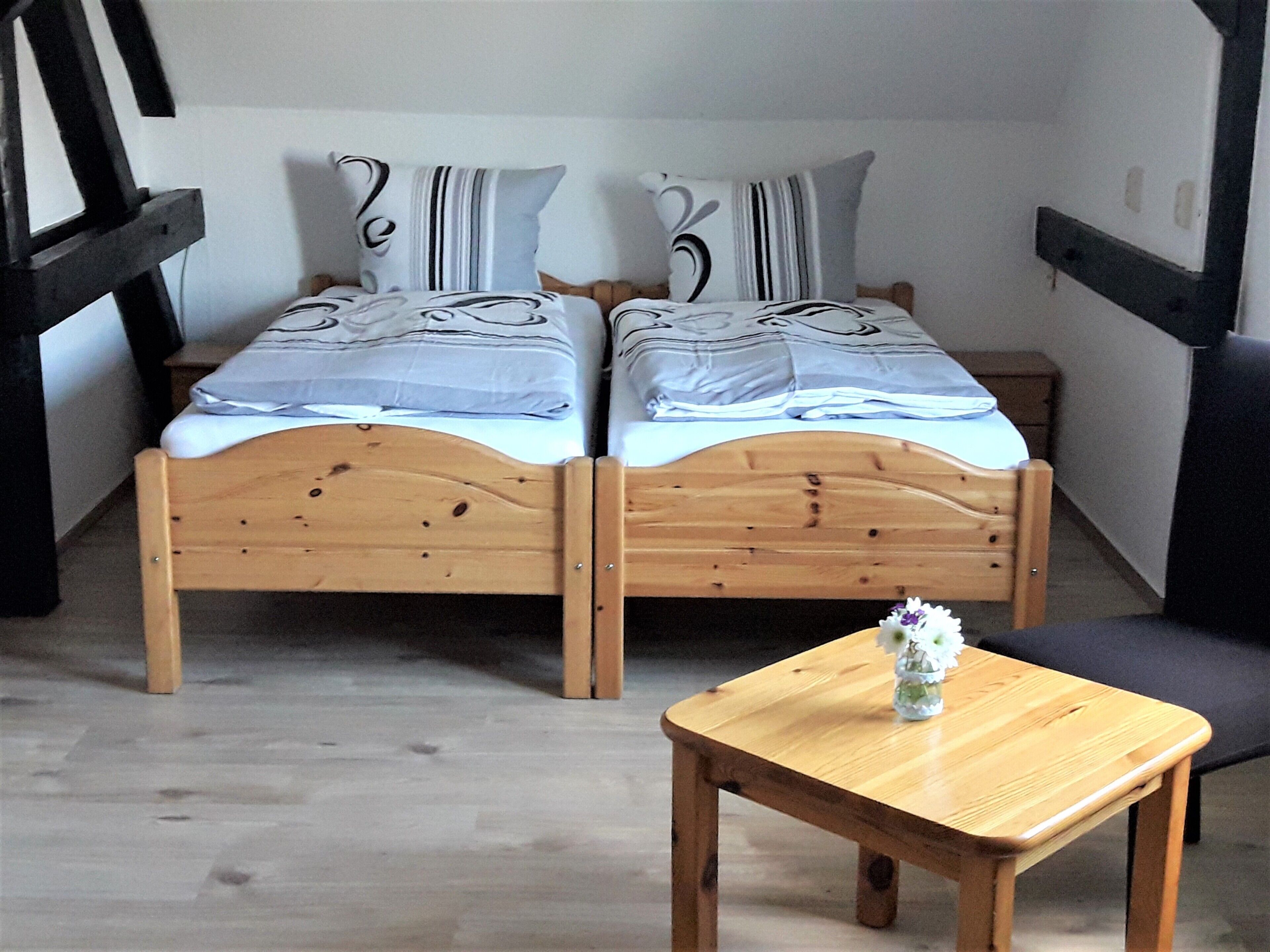 Ein Doppelbett mit gestreifter Bettwäsche, ein kleiner Holztisch mit einer Vase und ein Stuhl.