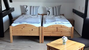 A double bed with striped bedding, a small wooden table with a vase, and a chair.