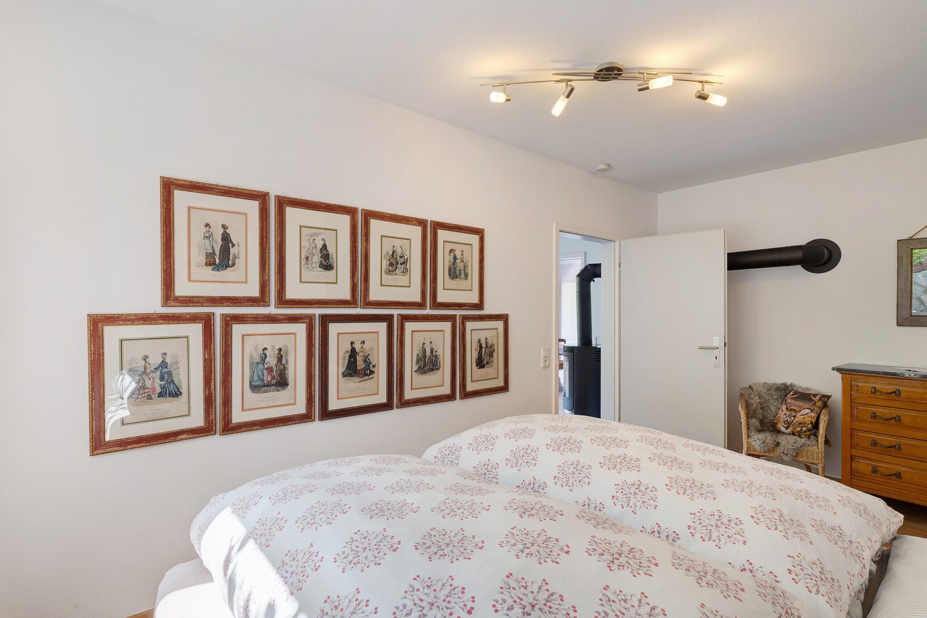 Ein Schlafzimmer mit einem Bett, einem Sessel, einer Kommode und gerahmten Bildern an der Wand.