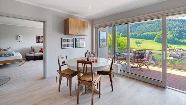 Un interno moderno con zona pranzo, divano e vista su un paesaggio verde attraverso ampie finestre.