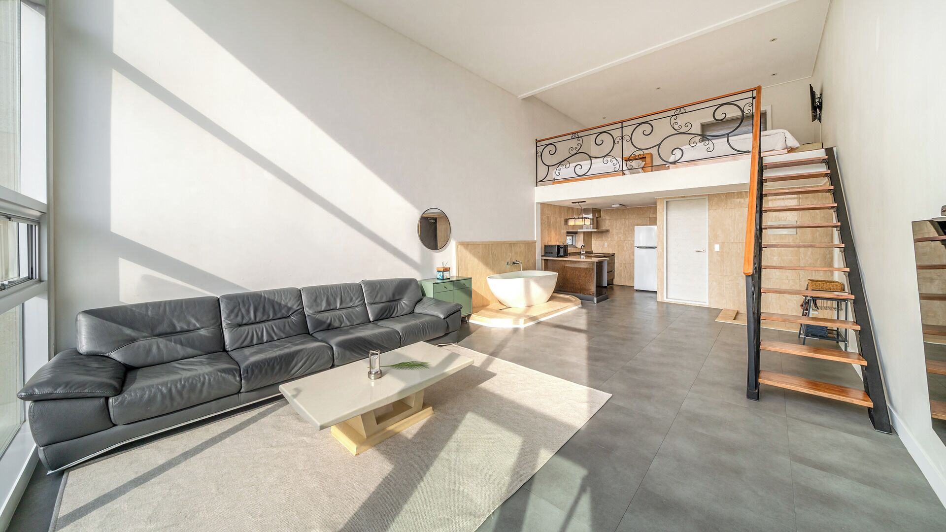A spacious living area with a leather sofa, a coffee table, and a view of the kitchen and upper floor.