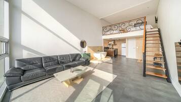 A spacious living area with a leather sofa, a coffee table, and a view of the kitchen and upper floor.