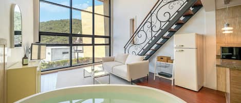 A modern interior with a sofa, a glass-top table, a white refrigerator, and a staircase with a decorative railing.