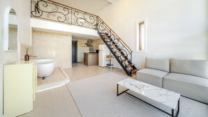 Una sala de estar moderna con un sofá blanco, una mesa de centro de mármol, una zona de cocina con refrigerador y una escalera con barandilla decorativa.