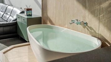 Un baño moderno con una bañera independiente, una mesita de noche verde y un sofá de cuero.