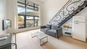 Una sala de estar con un sofá, una mesa de centro, un televisor, una escalera y un refrigerador.