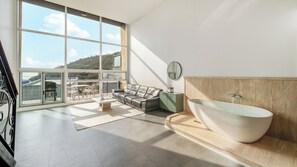 Un baño moderno con una bañera independiente, un sofá y una zona de comedor con vistas a las colinas.