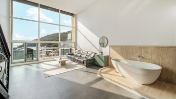 Un baño moderno con una bañera independiente, un sofá y una zona de comedor con vistas a las colinas.