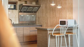 Cocina moderna con una isla central, electrodomésticos de acero inoxidable y un taburete blanco.