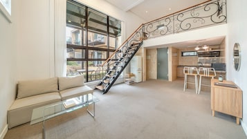 Amplia sala de estar con una escalera moderna, una mesa de centro de vidrio y una zona de cocina con barra.