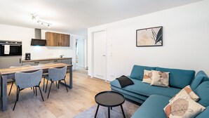 Una sala de estar moderna con sofá, sillas, una mesa de centro y una zona de cocina con mesa de comedor.
