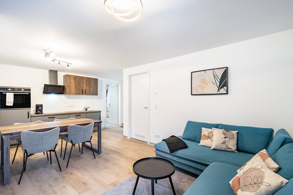 Una sala de estar moderna con sofá, sillas, una mesa de centro y una zona de cocina con mesa de comedor.