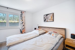 Un dormitorio con dos camas individuales, cabecero de madera, una mesita de noche con lámpara y una ventana con cortinas.