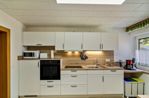 Une cuisine moderne avec des meubles blancs, un four à micro-ondes, un four traditionnel, un évier et une fenêtre avec des rideaux.