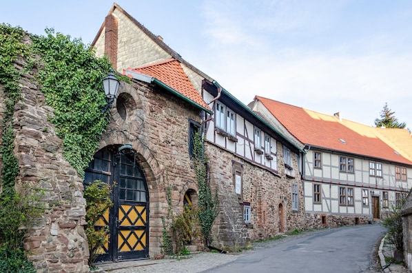 Un bâtiment historique en pierre, doté d’une porte noire, d’une structure adjacente à colombages et situé le long d’une rue pavée.