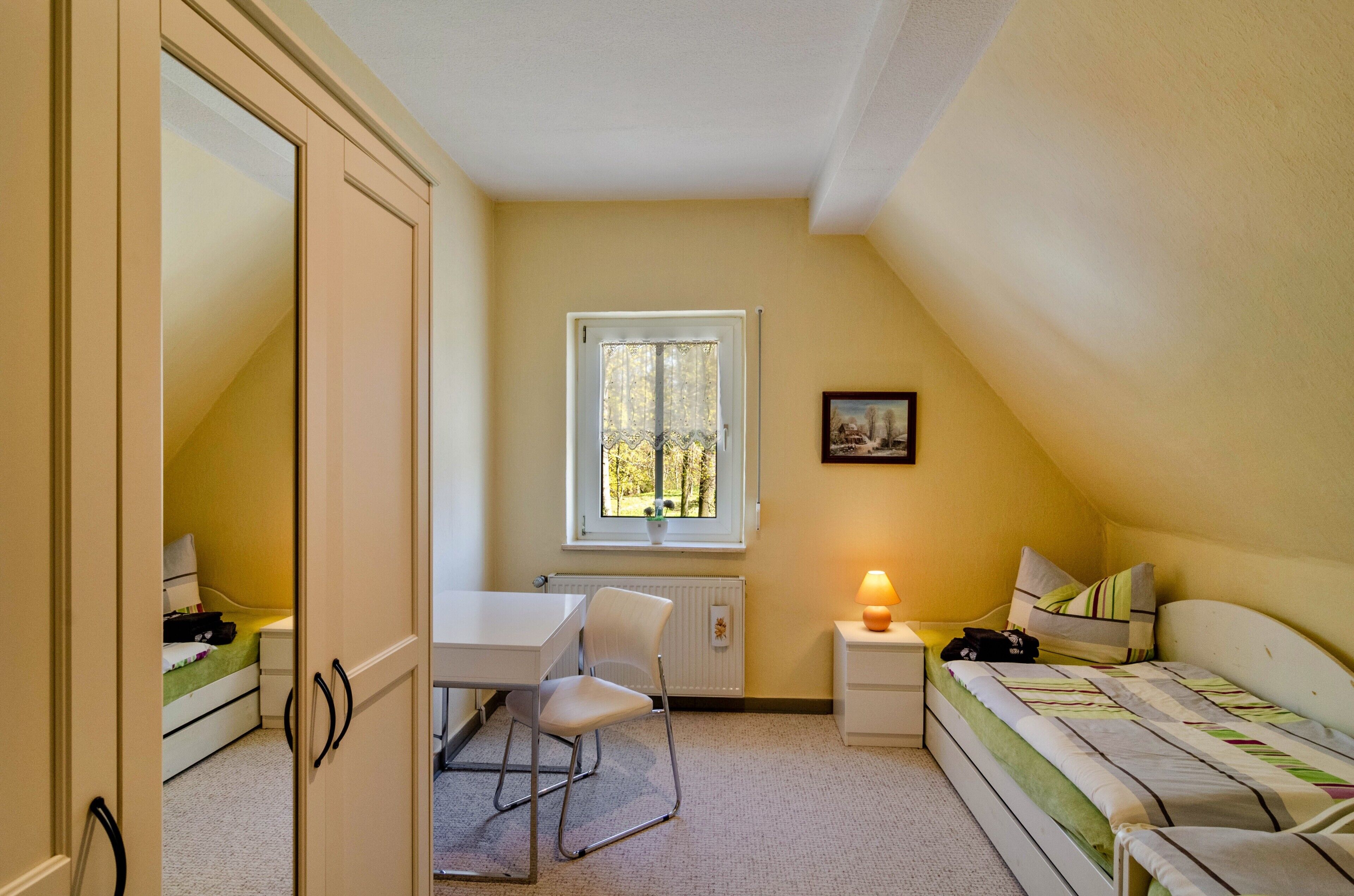 Une chambre à coucher avec un lit, un bureau, une chaise, une fenêtre et un radiateur.