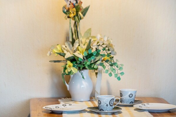 Ein Tisch mit einer weißen Karaffe, zwei Tassen und Tellern vor einer schlichten Wand.