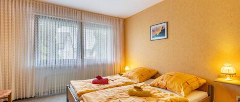 A hotel room with two beds, a chair, a lamp, and a painting on the wall.
