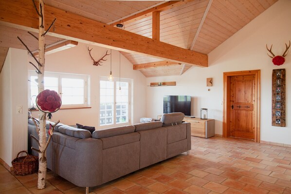 Una sala de estar con un sofá seccional grande, techo de madera y televisor.