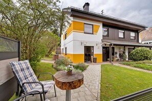 A modern two-story house with a yellow and white exterior, a paved patio, and a wooden table with a flower vase. - Apartment 'Peaceful Living in Sulz' with Balcony and Wi-Fi (Sulz am Neckar)