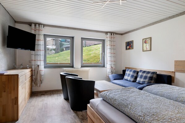 A modern room with a bed, a sofa, a TV, and two windows. - Apartment 'Peaceful Living in Sulz' with Balcony and Wi-Fi (Sulz am Neckar)
