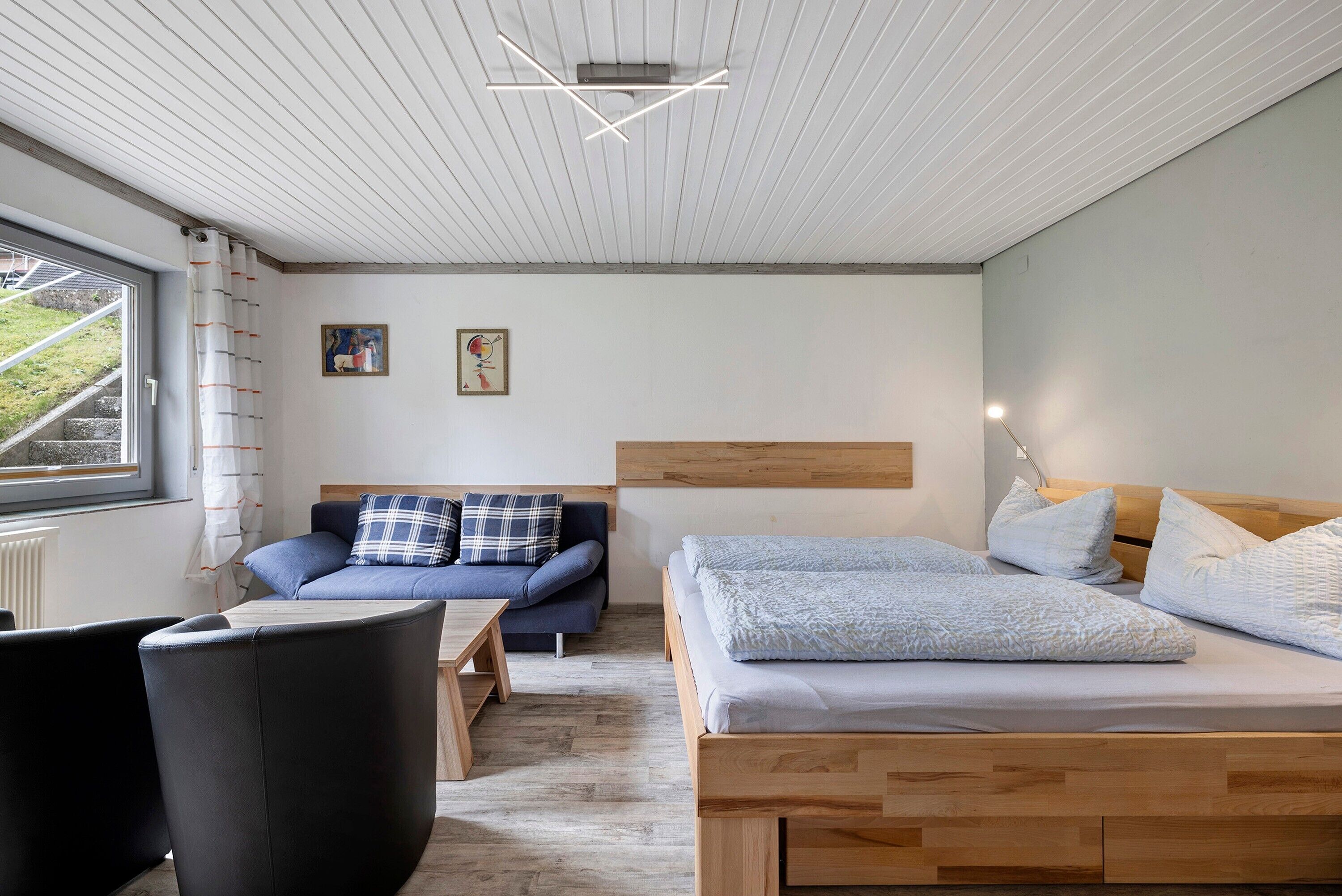 A modern bedroom with a wooden bed, a sofa, a chair, and a small table.