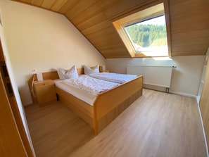 Une chambre avec un plafond en pente, une fenêtre donnant sur les arbres, un lit avec une literie blanche et un plancher en bois.