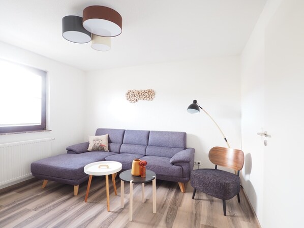 En moderne stue med sofa, rundt sofabord, et sengebord, gulvlampe og dekorativt vægkunstværk.
