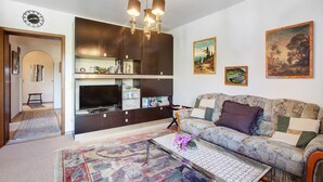 Een woonkamer met een bank, een salontafel, een televisie en een kroonluchter.