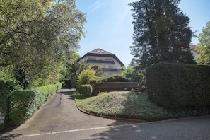 A residential street with a house, hedges, and a clear sky.