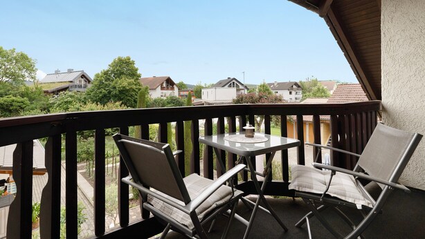 A balcony with two chairs and a small table, overlooking a residential area.