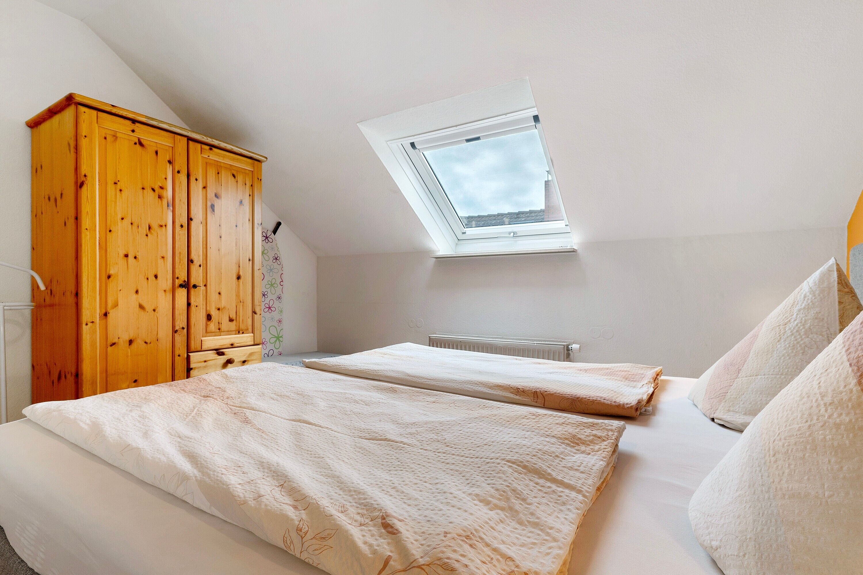 Ein Schlafzimmer mit einem Oberlicht, einem Holzschrank, zwei Betten und einer Heizung.